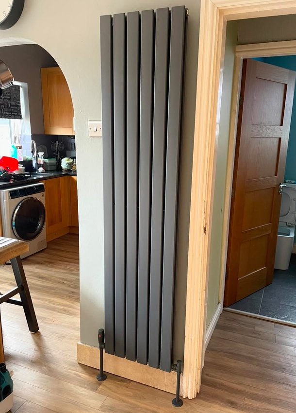 Tall anthracite radiator mounted beside an internal doorway