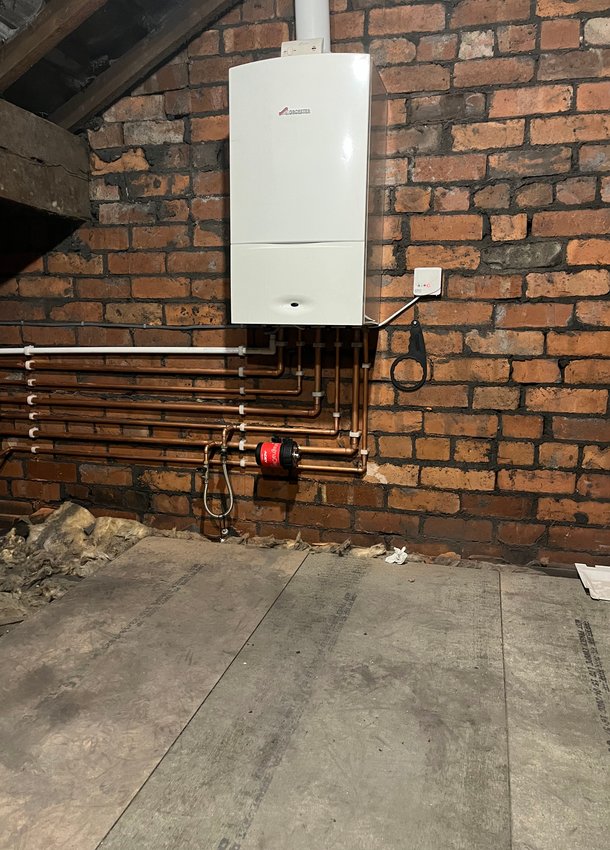 White boiler and copper pipework against an exposed brick wall