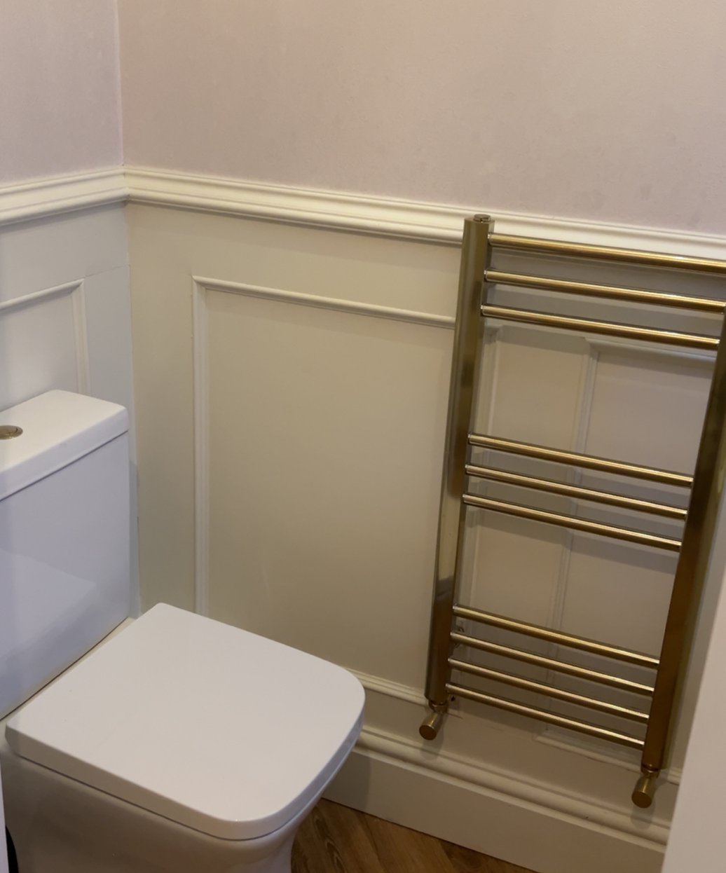 Brushed brass towel radiator beside a toilet in a panelled bathroom