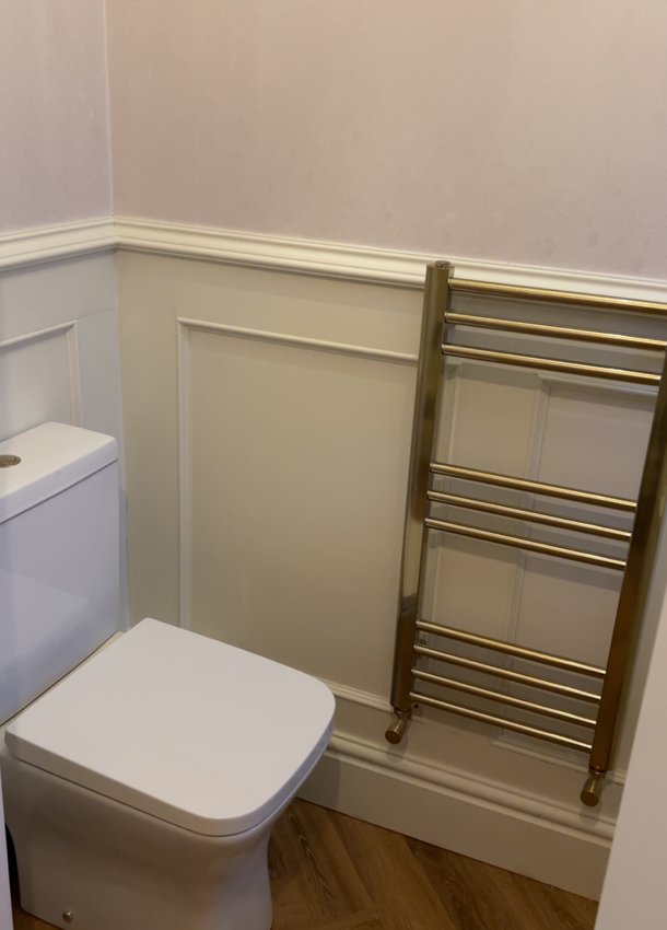 Brushed brass towel radiator beside a toilet in a panelled bathroom
