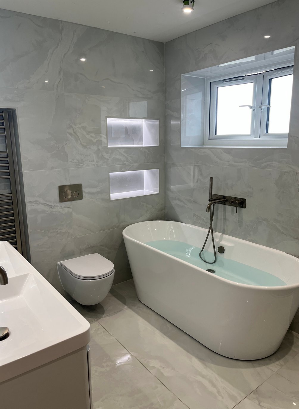 Grey bathroom with a freestanding bath, wall-hung toilet and illuminated niches