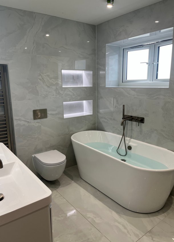 Grey bathroom with freestanding bath, wall-hung toilet and illuminated niches