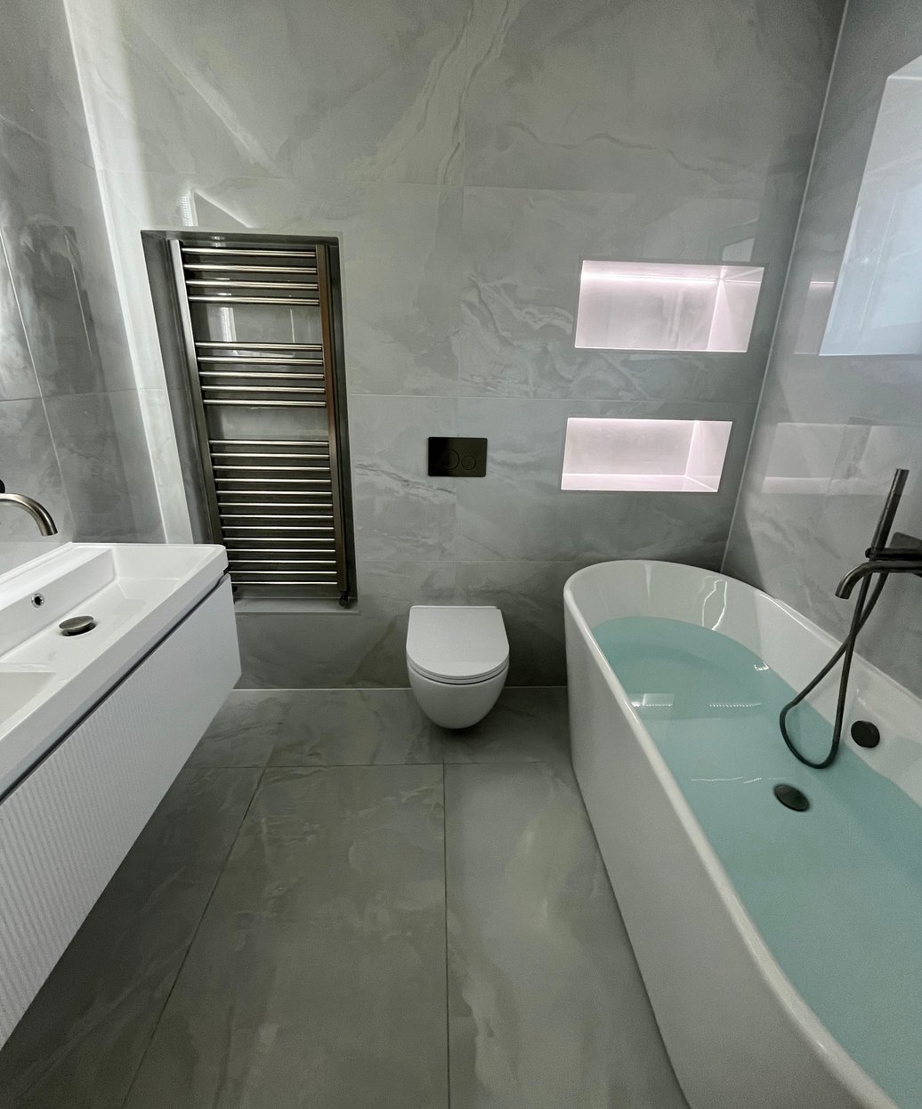 Grey bathroom with a vanity, wall-hung toilet and illuminated niches
