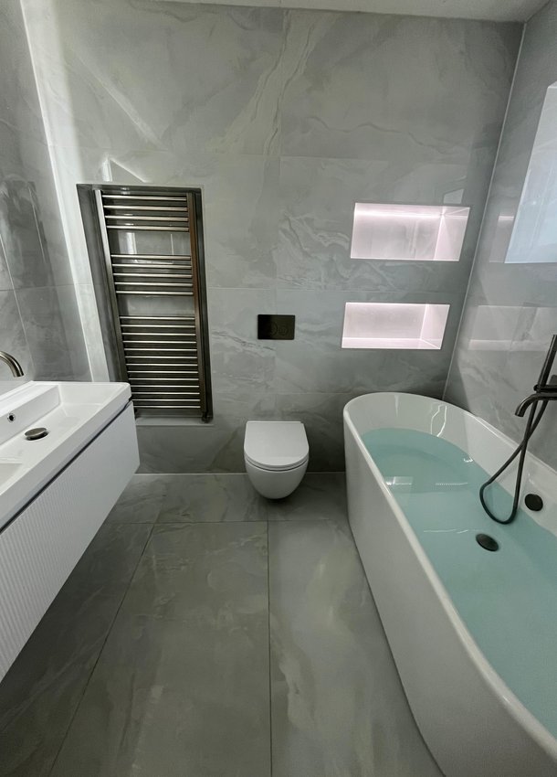 Grey bathroom with vanity, wall-hung toilet, bath, towel radiator and illuminated niches
