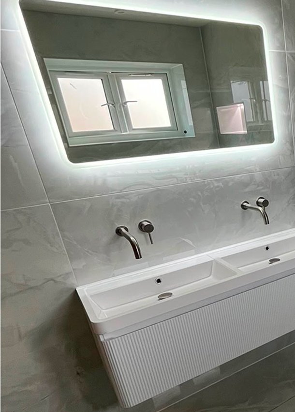 Grey bathroom with twin basins, illuminated mirror and chrome towel radiator