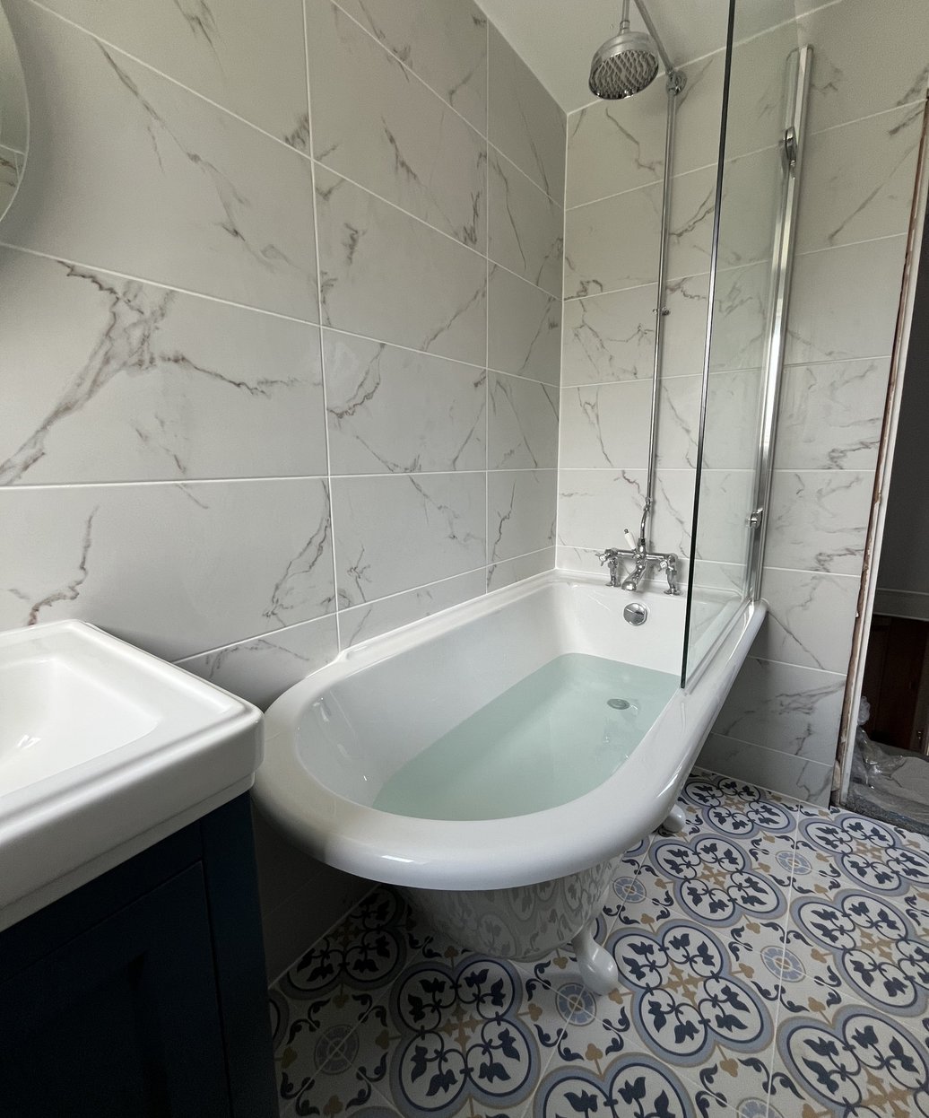 Bathroom with a roll-top bath, rainfall shower and patterned floor tiles
