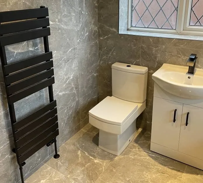Modern bathroom installation in Bolton featuring a white toilet, vanity unit, and black heated towel rail