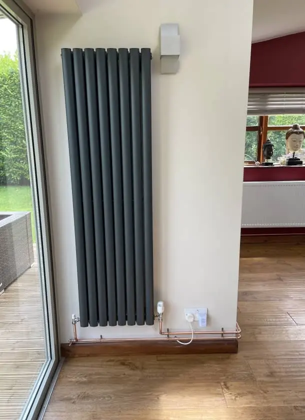 Tall grey vertical radiator installed on living room wall