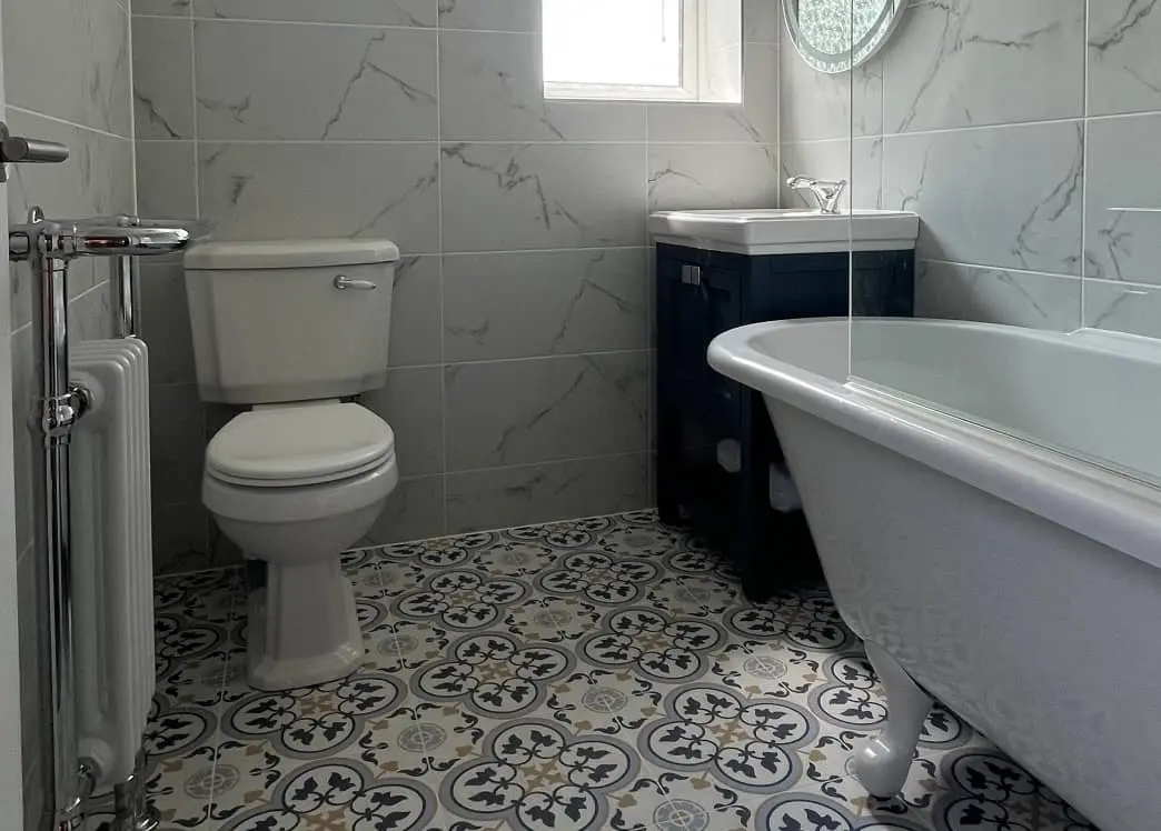 Traditional bathroom installation in Bolton with freestanding roll-top bath, patterned tile flooring, and white ceramic toilet and basin