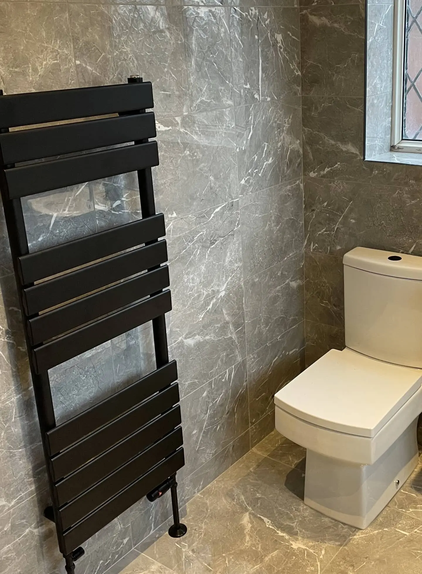 Modern bathroom installation in Bolton featuring grey tiled walls, white toilet, vanity unit, and black towel radiator